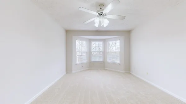 an empty room with a chandelier fan and windows