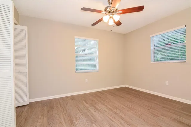 an empty room with wooden floor fan and windows