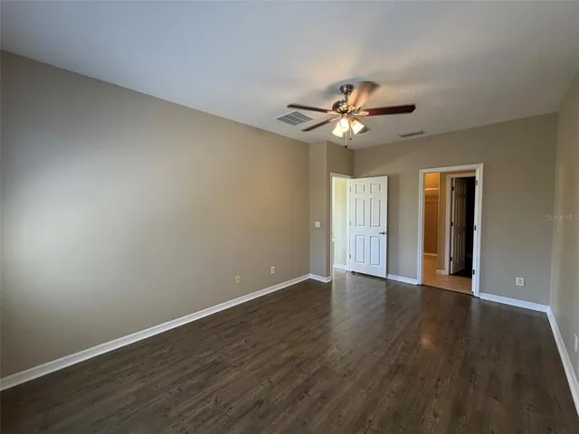 a view of an empty room with window a ceiling fan and wooden floor