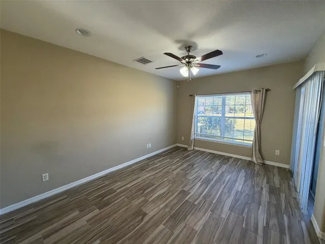 an empty room with wooden floor fan and windows