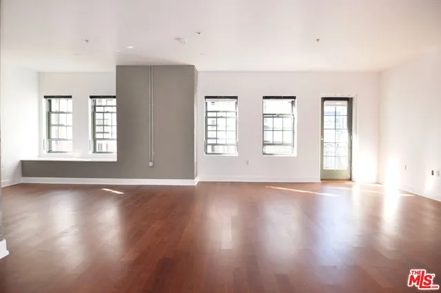 a view of an empty room with wooden floor and window