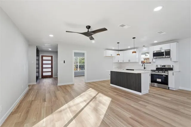 a large white kitchen with stainless steel appliances kitchen island a sink dishwasher a stove and a refrigerator with wooden floor