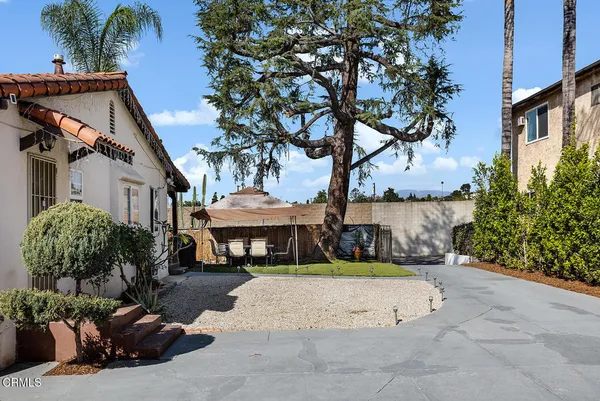 a view of a white house with a large tree and a yard with plants