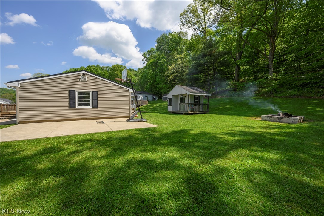 6105 Wolf Run Road Southeast Dennison, OH 44621 - Photo 5 of 35 Expansive green space featuring a concrete patio, a detached shed with a porch, a built-in fire pit, and a backdrop of mature trees