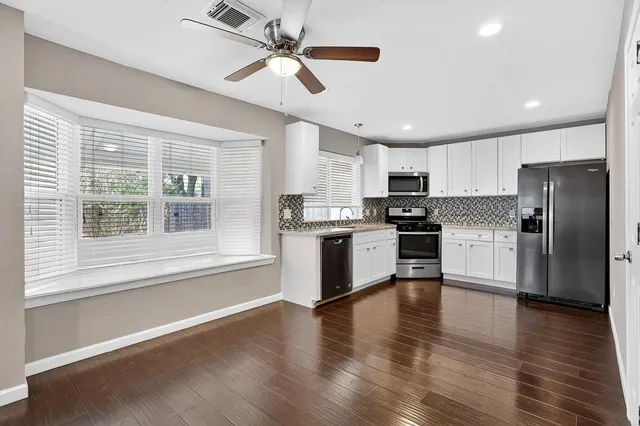 a kitchen with stainless steel appliances granite countertop a refrigerator a sink dishwasher a stove and white countertops with wooden floor