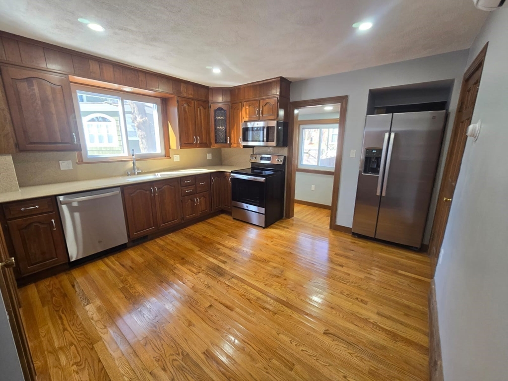 22 Linden Street Reading, MA 01867 - Photo 11 of 32 a large kitchen with stainless steel appliances granite countertop a refrigerator a sink dishwasher a stove and white countertops with wooden floor