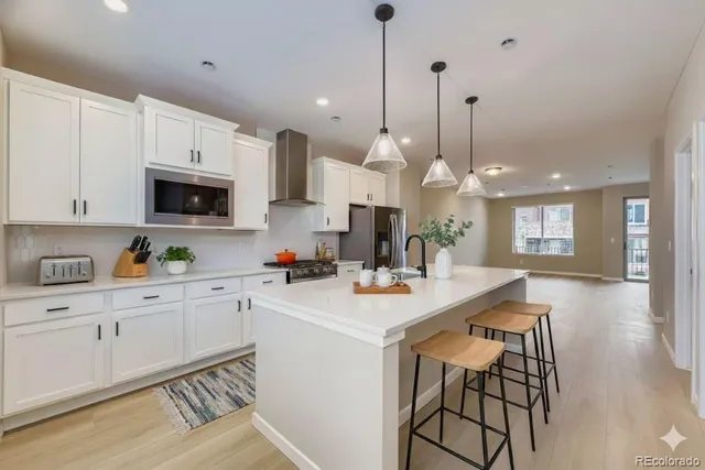 a kitchen with stainless steel appliances kitchen island granite countertop a sink a stove a dining table and chairs with wooden floor