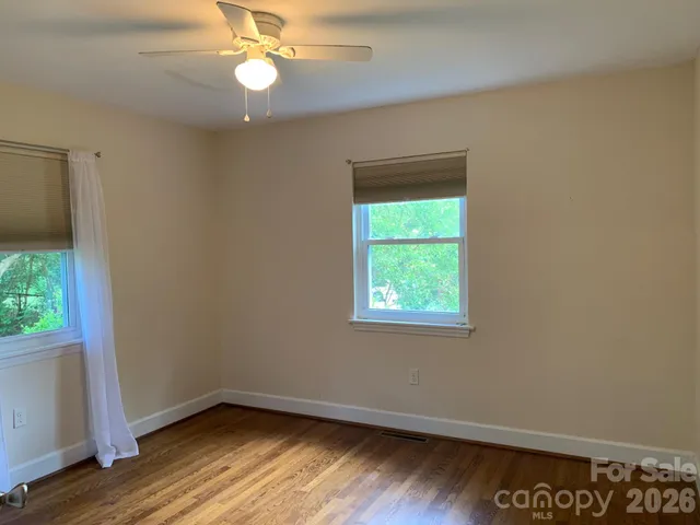 an empty room with wooden floor fan and window
