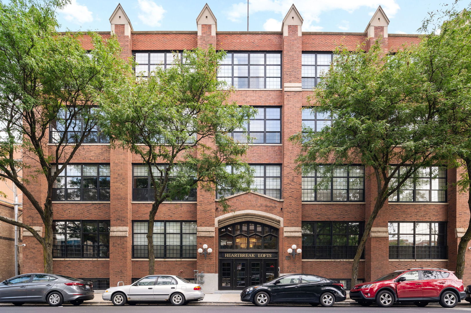 a front view of a building with lot of cars and trees