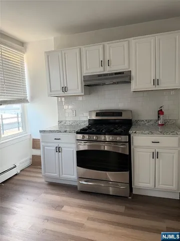 a kitchen with granite countertop white cabinets and a stove a sink