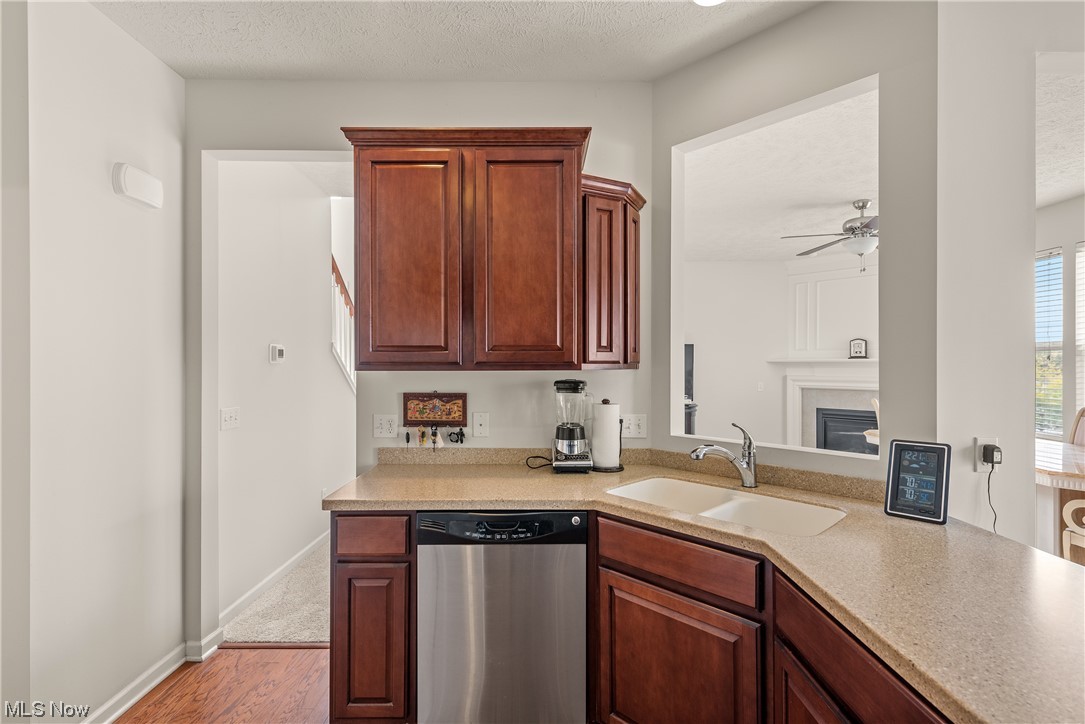 3967 Gardiner Run Akron, OH 44321 - Photo 11 of 35 Kitchen featuring stainless steel dishwasher, a textured ceiling, a fireplace, light countertops, light hardwood flooring, and ceiling fan