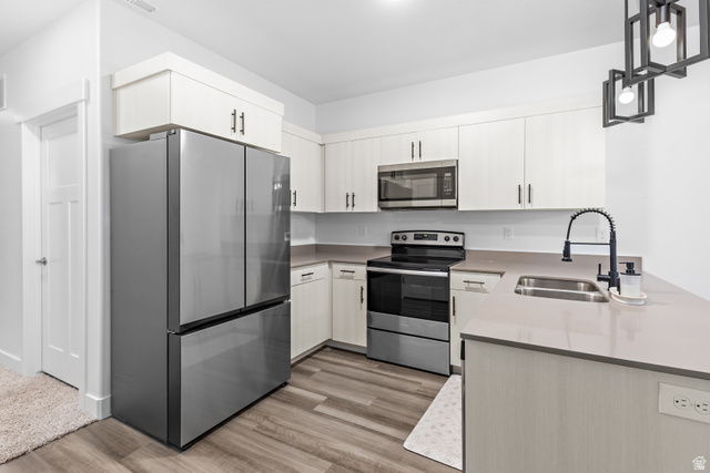 4735 Alder Drive, Unit F101 Mapleton, UT 84664 - Photo 11 of 30 Kitchen with stainless steel appliances, hanging light fixtures, a peninsula, light wood-style flooring, and light stone counters