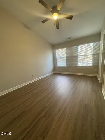 an empty room with wooden floor fan and windows
