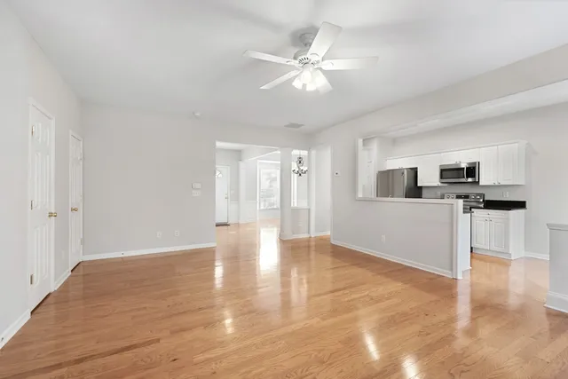 a view of an empty room with kitchen and window