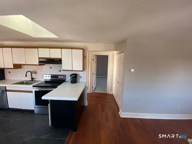 a kitchen with stainless steel appliances granite countertop a sink dishwasher a stove a refrigerator and white cabinets with wooden floor