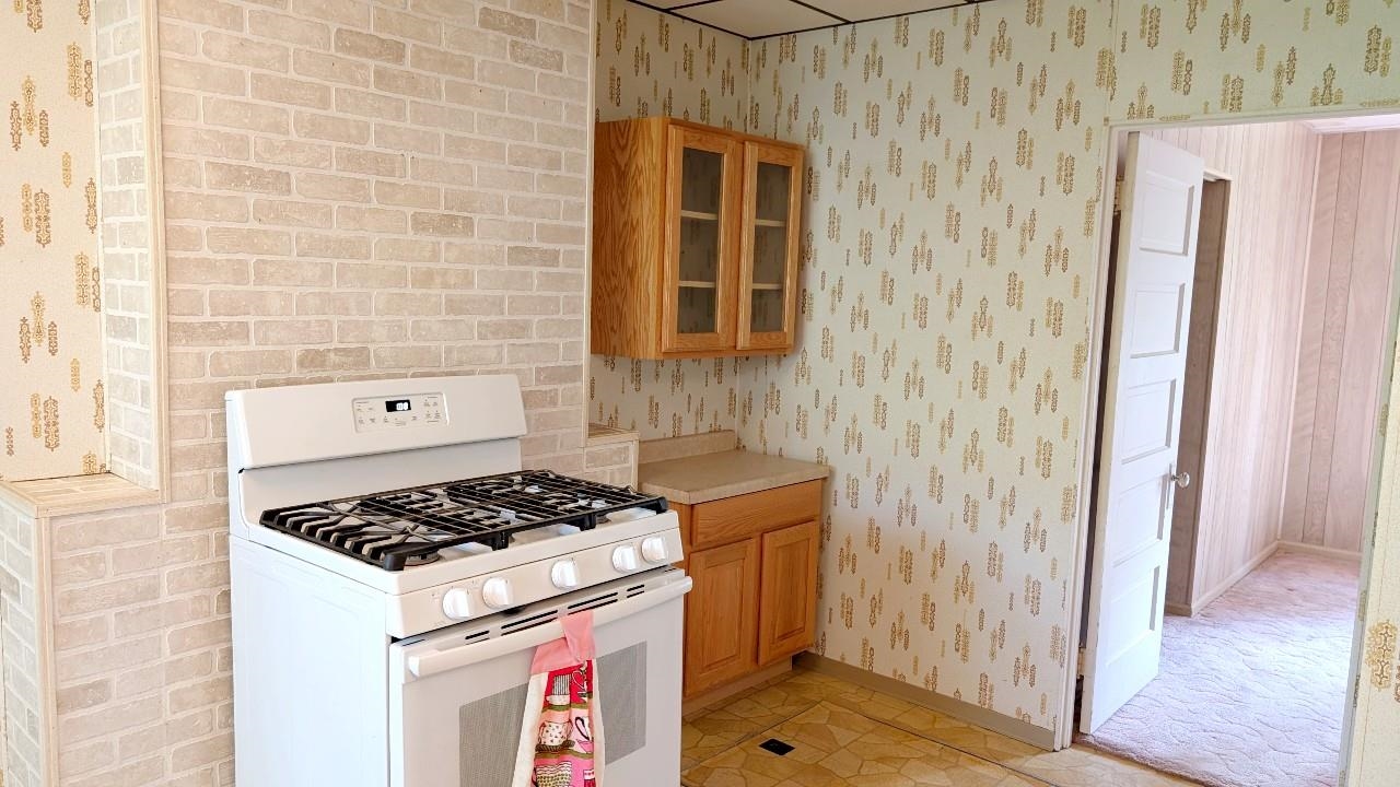 8159 Ludlow Road Cook, MN 55723 - Photo 14 of 32 Kitchen with white gas range oven, light countertops, wallpapered walls, brown cabinets, and glass insert cabinets