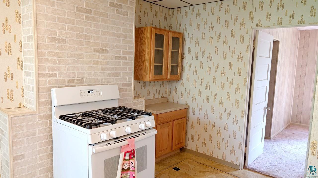 8159 Ludlow Road Cook, MN 55723 - Photo 14 of 32 Kitchen with white gas range oven, light countertops, wallpapered walls, brown cabinets, and glass insert cabinets