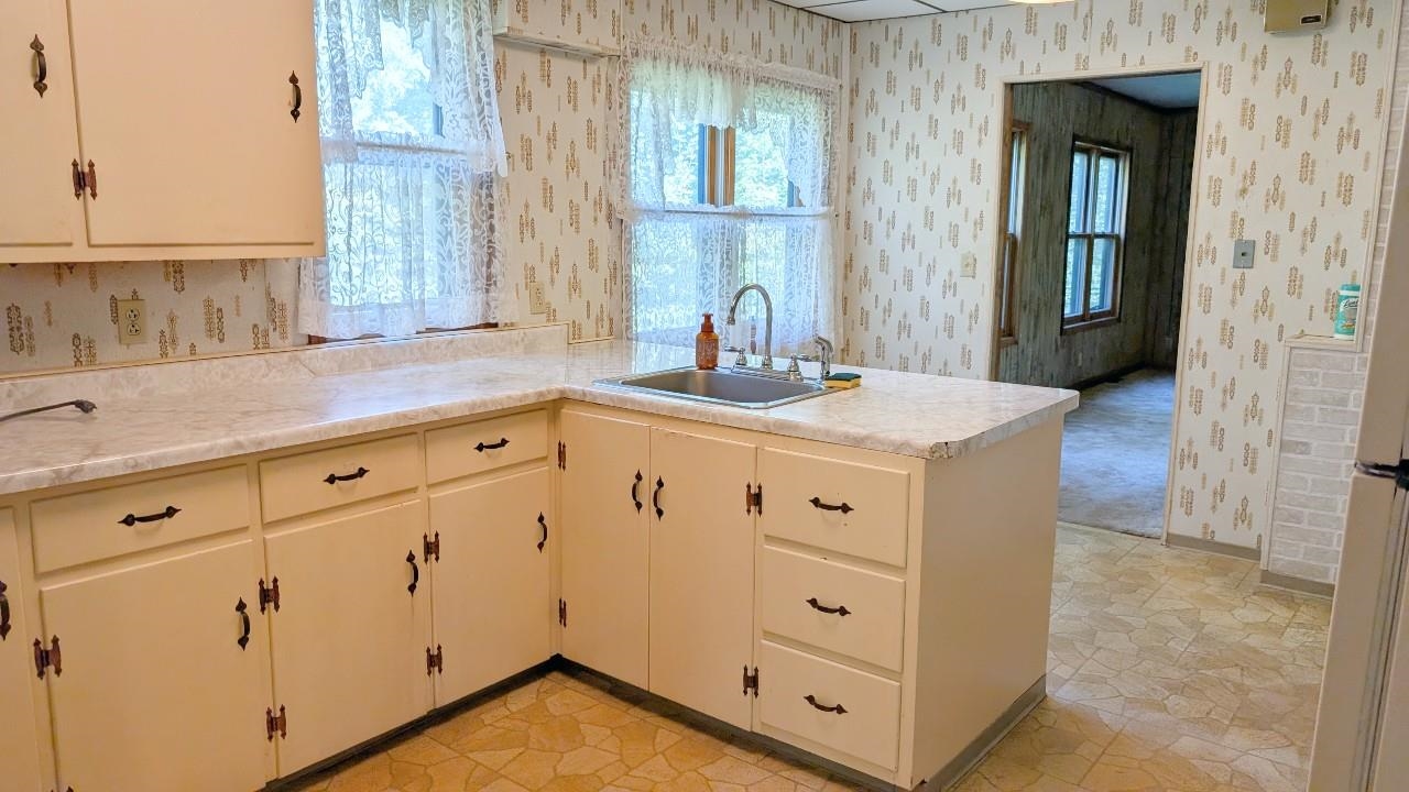 8159 Ludlow Road Cook, MN 55723 - Photo 4 of 32 Kitchen featuring light countertops, wallpapered walls, a peninsula, freestanding refrigerator, and white cabinetry