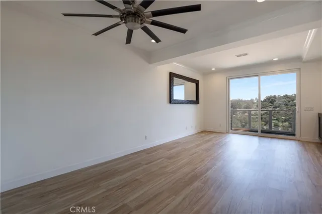 an empty room with wooden floor fan and windows