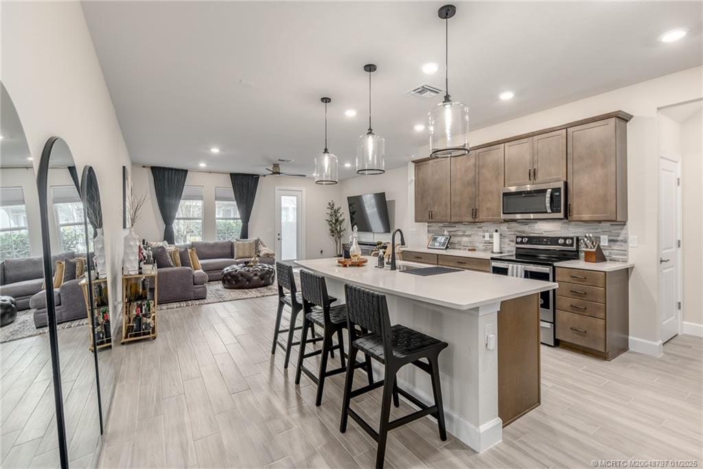 1865 Southeast Tarni Way Stuart, FL 34996 - Photo 3 of 23 a kitchen with stainless steel appliances kitchen island granite countertop a stove a sink a oven a dining table and chairs with wooden floor