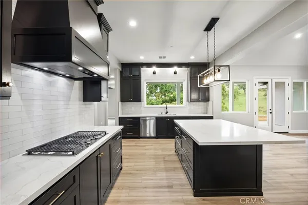 a large kitchen with stainless steel appliances a large counter top a stove a chimney a sink and a refrigerator