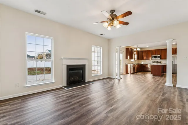 an empty room with wooden floor a kitchen view and a fireplace