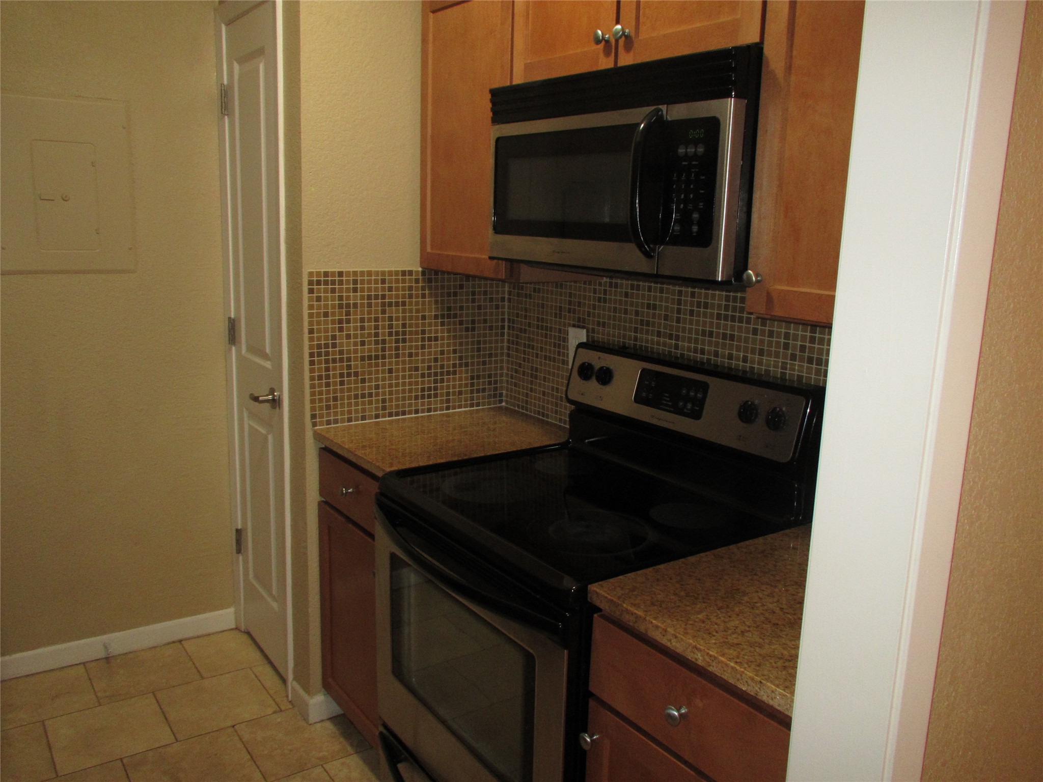 3204 Menchaca Road, Unit 702 Austin, TX 78704 - Photo 7 of 14 Kitchen with stainless steel appliances, wood finish cabinets, electric panel, light tile patterned floors, and backsplash