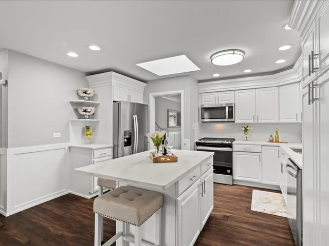 a kitchen with stainless steel appliances a stove a sink dishwasher a refrigerator white cabinets and wooden floor