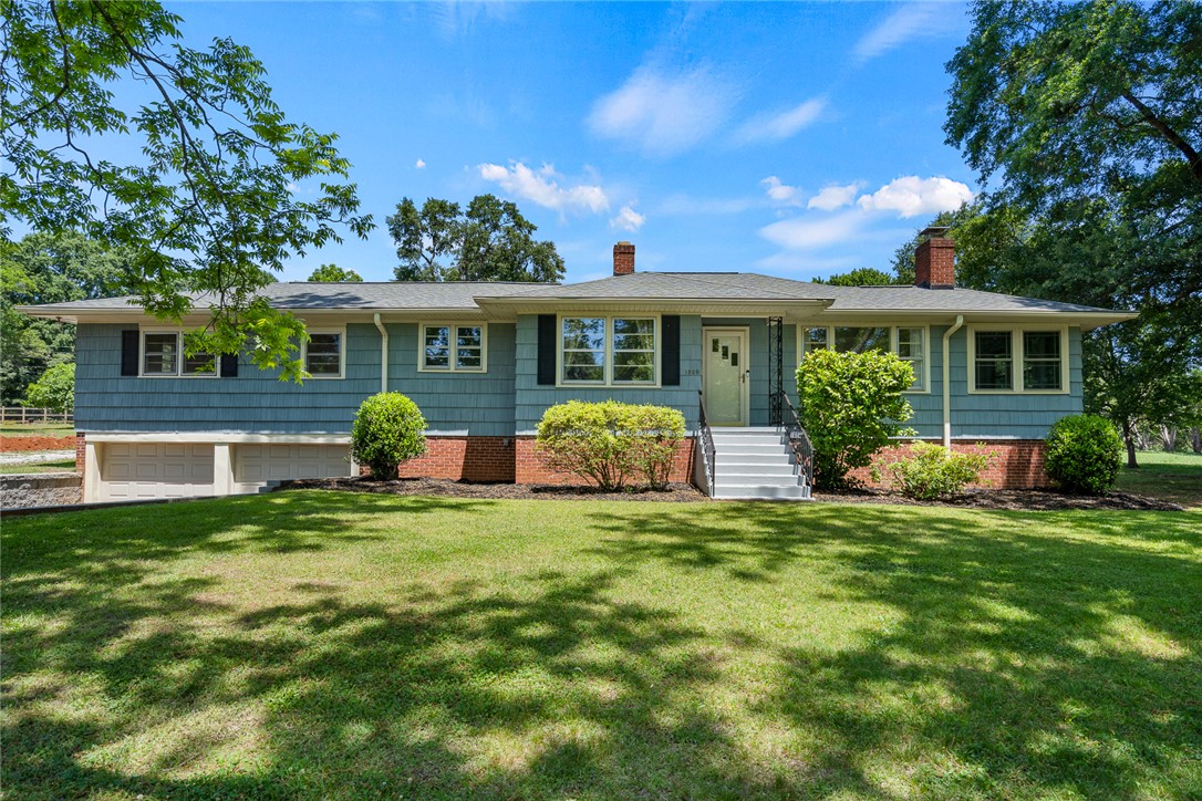 1509 869 Anderson, SC 29621 - Photo 2 of 45 A classic ranch home, distinguished by a warm brick foundation and light blue siding, sits amidst lush green landscaping.
