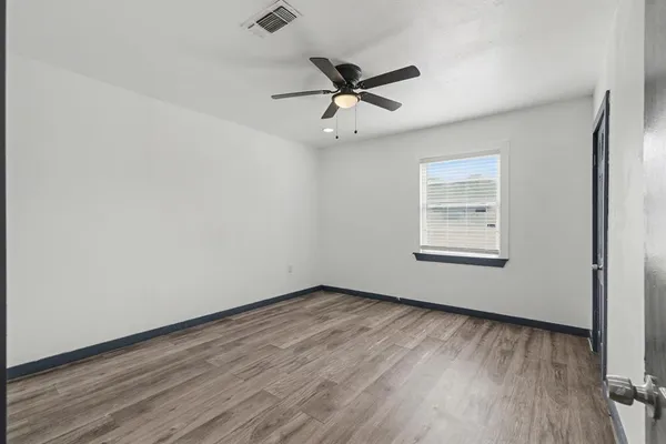 an empty room with wooden floor ceiling fan and windows