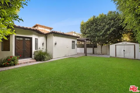 a backyard of a house with plants and large tree