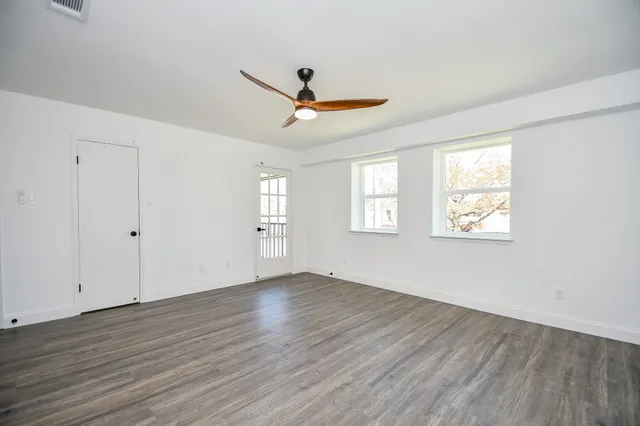 an empty room with wooden floor ceiling fan and windows