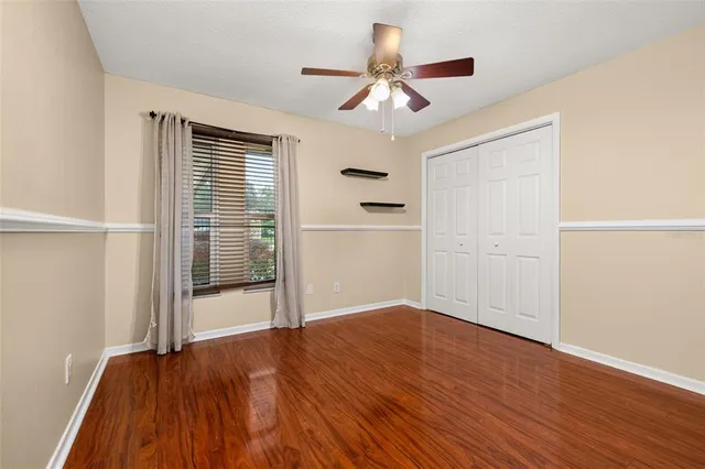 an empty room with wooden floor chandelier fan and windows