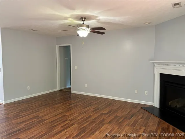 a view of an empty room with wooden floor fireplace and a window