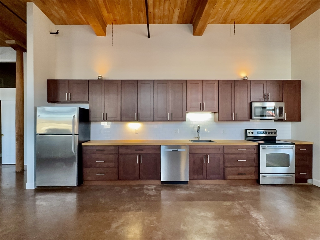 35 Riverwalk Way, Unit R302 Lowell, MA 01854 - Photo 3 of 20 a kitchen with granite countertop a refrigerator stove top oven and cabinets