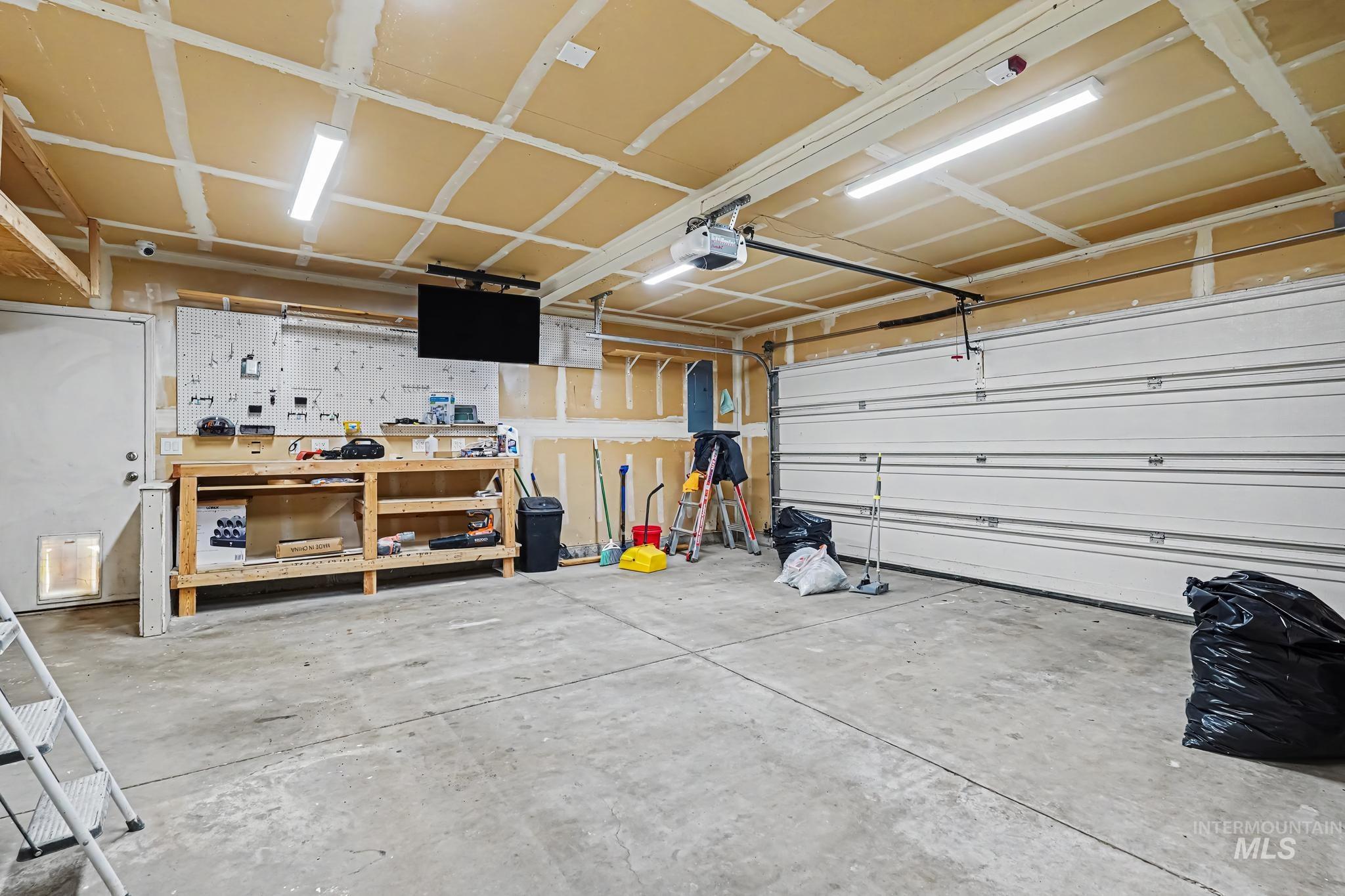 14421 West Stockwell Street Boise, ID 83713 - Photo 11 of 20 Spacious garage featuring a concrete floor, built-in workbench, overhead shelving, and an automatic garage door opener