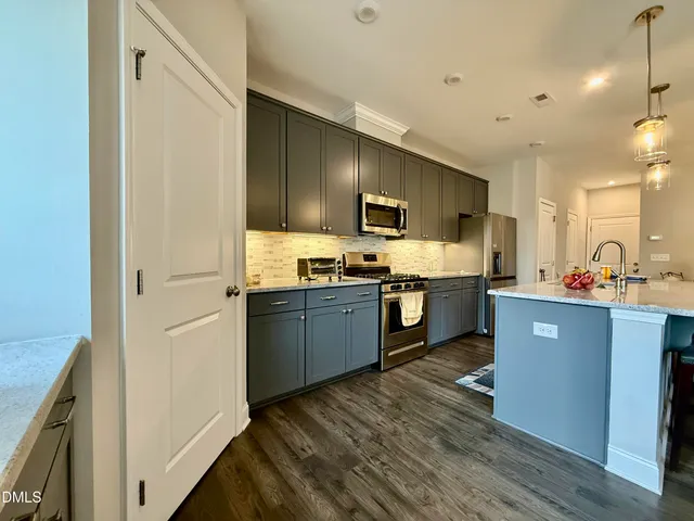 a kitchen with stainless steel appliances granite countertop a refrigerator a sink dishwasher a stove top oven a kitchen island and chairs with wooden floor