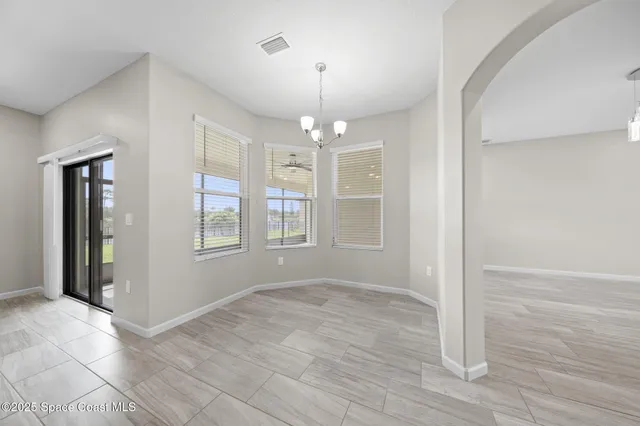 an empty room with wooden floor chandelier fan and windows