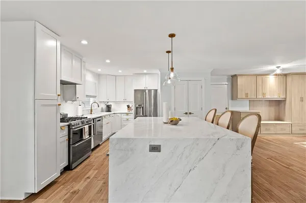 a large kitchen with kitchen island a stove a sink a refrigerator and white cabinets with wooden floor