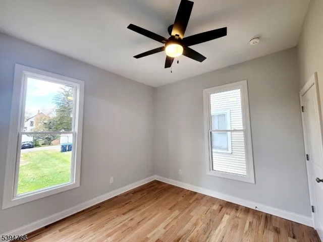 an empty room with wooden floor fan and windows