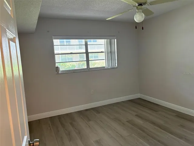 an empty room with wooden floor fan and windows