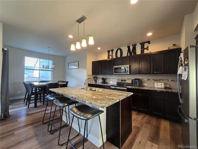 a kitchen with stainless steel appliances kitchen island granite countertop a table chairs and a refrigerator