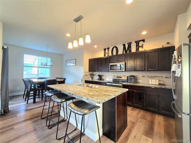 a kitchen with stainless steel appliances granite countertop a stove top oven a sink dishwasher a dining table and chairs with wooden floor