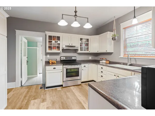 a kitchen with stainless steel appliances granite countertop a sink a stove a refrigerator cabinets and a window