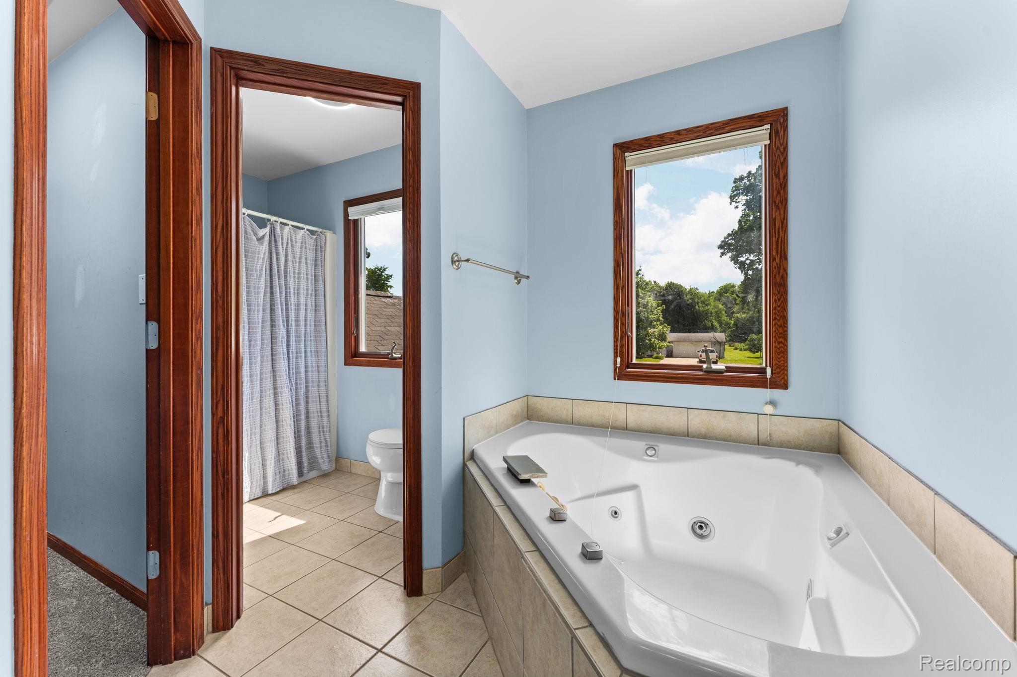 2381 Burke Road Fowlerville, MI 48836 - Photo 16 of 31 Corner jetted tub featuring a tiled surround and an adjacent window with wood trim