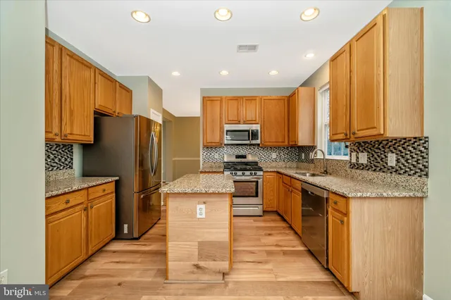 a kitchen with stainless steel appliances granite countertop a stove top oven a refrigerator a sink and dishwasher a oven with wooden cabinets