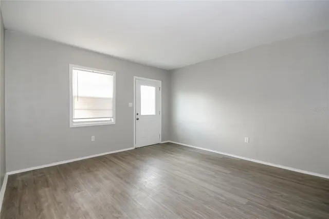 a view of an empty room with wooden floor and a window