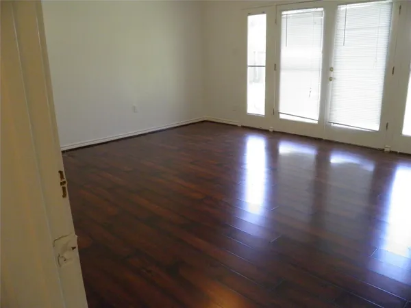 an empty room with wooden floor and windows with curtains