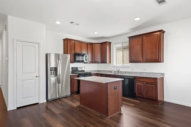 a kitchen with stainless steel appliances granite countertop a refrigerator a stove top oven a sink and dishwasher with wooden floor