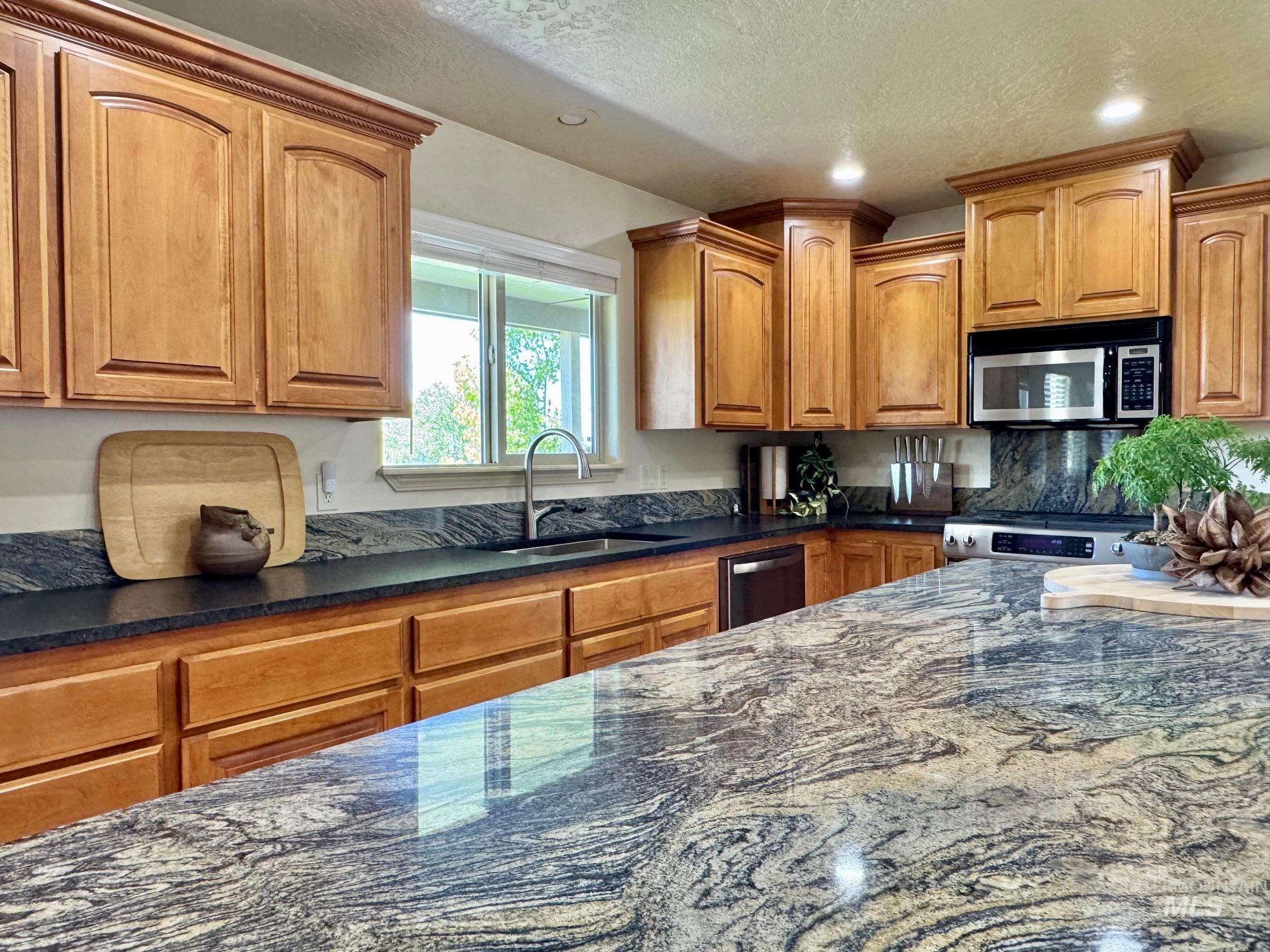 9299 Kemp Road Middleton, ID 83644 - Photo 11 of 50 Expansive kitchen featuring a large island with patterned stone countertop, wood cabinetry, stainless steel appliances, a built-in microwave, and a window above the sink